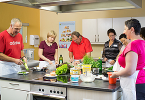 Personen in einer Küche, welche gemeinsam Zutaten vorbereiten.